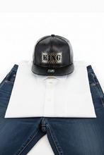 Load image into Gallery viewer, A black snapback cap with a metal patch that reads 'KING' on the front, featuring a textured design and a flat visor.